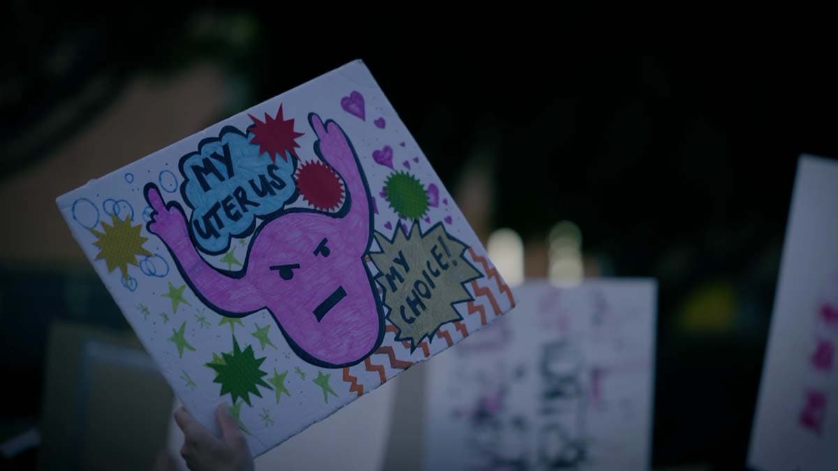 A picket sign held up during a protest. The sign has a drawing of a uterus holding up two middle fingers, with the words, "My uterus, my choice!"